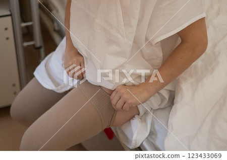 A woman puts on post-operative compression stockings in a hospital room.  123433069