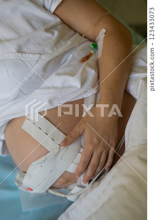 Close up of pregnant woman belly with cardiotocography sensor and IV in vein in delivery room.  123433073