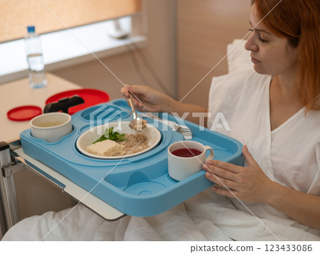 Caucasian woman eating on hospital bed.  123433086