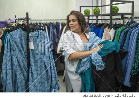 A fat woman chooses clothes in a plus size store.  123433133