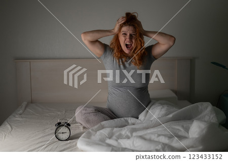 Caucasian pregnant woman sitting in bed and screaming while suffering from insomnia.  123433152