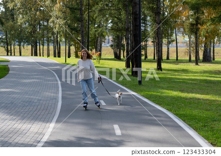 Caucasian woman roller skating with her jack russell terrier dog in park. Caucasian woman roller skating with her jack russell terrier dog in park. 123433304