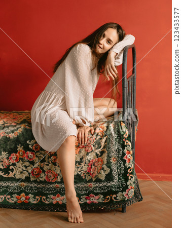 Cheerful woman with natural flawless skin, wearing vintage style dress sitting on retro bed. Cheerful woman with natural flawless skin, wearing vintage style dress sitting on retro bed. 123433577