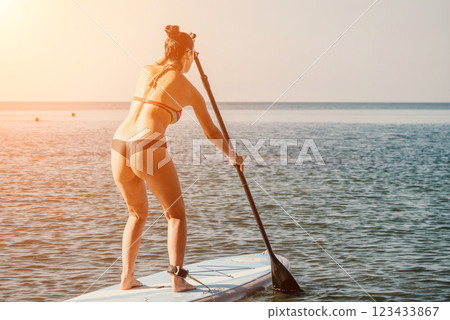 Sea woman sup. Silhouette of happy middle aged tanned woman in rainbow bikini, surfing on SUP board, confident paddling through water surface. Idyllic sunset. Active lifestyle at sea or river. 123433867