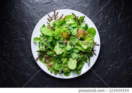White plate filled with mix of fresh salad greens on black background 123434354