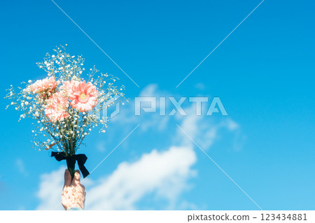 藍天下，一手捧著一束粉紅色非洲菊和滿天星 123434881
