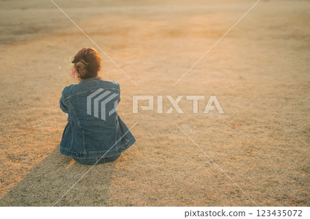 傍晚，一位身穿牛仔服的女士坐在公園的草地上 123435072