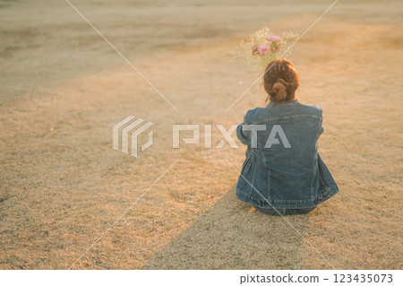 傍晚，一位身穿牛仔服的女士坐在公園的草地上 123435073