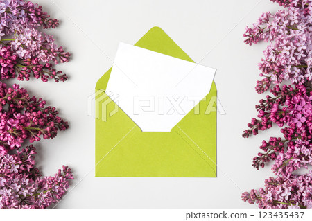Green envelope with clean white sheet of paper for your text and spring flowers purple lilac on gray background. Invitation to the holidays. Flat lay. Green envelope with clean white sheet of paper for your text and spring flowers purple lilac on gray background. Invitation to the holidays. Flat lay. 123435437