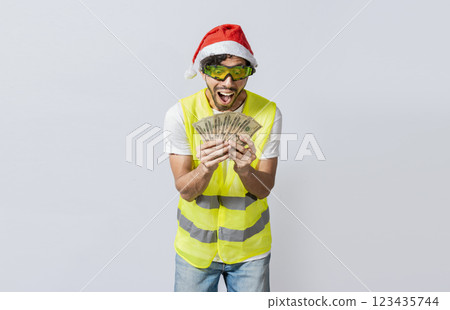Builder engineer in christmas hat with happy expression holding dollars isolated. Concept of engineer with money in holiday season, Engineer in christmas hat holding money smiling at camera 123435744