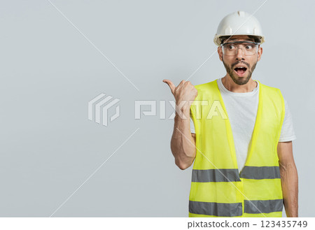 Surprised engineer pointing to the side. Surprised face construction worker pointing at an advertisement. Engineer man pointing to side. Surprised face engineer pointing finger to the right 123435749