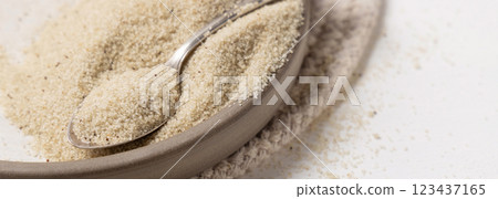 Raw uncooked fonio seeds on a plate with a metal spoon on white table. African ancient pseudocereal 123437165