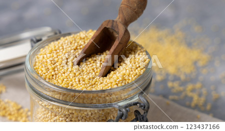 Glass jar of raw uncooked yellow millet grain with a wooden scoop closeup. Ancient food 123437166