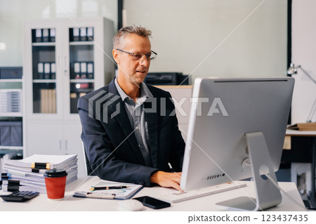 Mature male businessman working at office with laptop and documents on desk, financial adviser analyzing data. Mature male businessman working at office with laptop and documents on desk, financial adviser analyzing data. 123437435