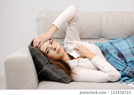 Portrait of young woman lying sick with the flu on sofa and touching head Portrait of young woman lying sick with the flu on sofa and touching head 123438723