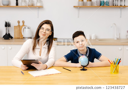A young woman helps a boy with his lessons using a tablet and a globe. A homeschooling student does his homework with the help of a tutor A young woman helps a boy with his lessons using a tablet and a globe. A homeschooling student does his homework with the help of a tutor 123438727
