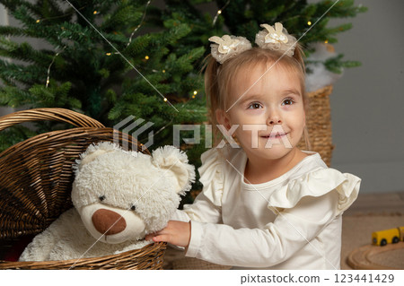 A funny little girl takes a fluffy teddy bear out of the basket in the Christmas room. 123441429