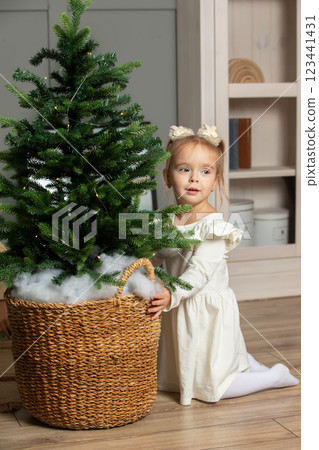 A little girl is looking at the Christmas tree in the room. 123441431