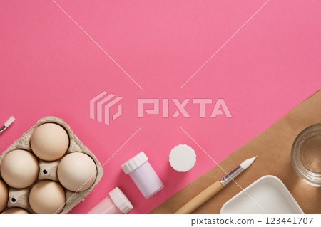 Easter egg painting preparation. Gouache for painting eggs, brushes, palette, glass of water on a pink background. A place for your text. 123441707