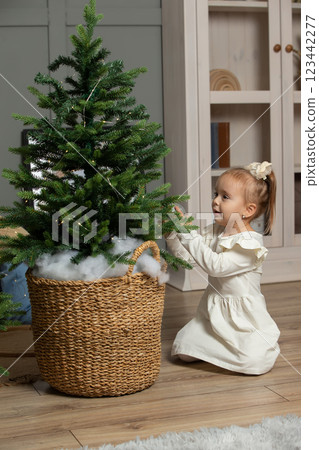 A little girl is looking at the Christmas tree in the room. A little girl is looking at the Christmas tree in the room. 123442277