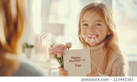 A little girl joyfully presents flowers and a card to her smiling mom in a sunlit room 123442365