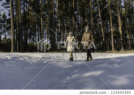 Elderly woman Nordic walking with a companion in a snowy forest on a sunny winter day. 123443393