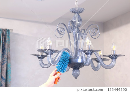 Woman wipe dust on glass chandelier with fluffy broom in living room. Cleanliness and order. Woman wipe dust on glass chandelier with fluffy broom in living room. Cleanliness and order. 123444390