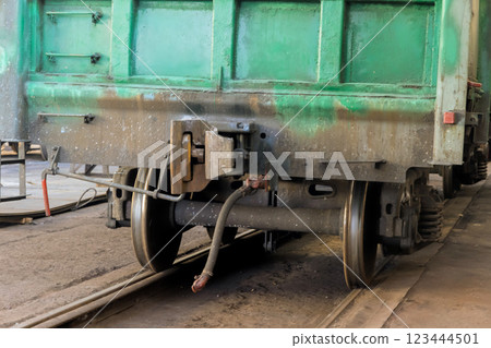 Green train wagon is under restoration on tracks inside railway workshop, showcasing its wheels construction. 123444501