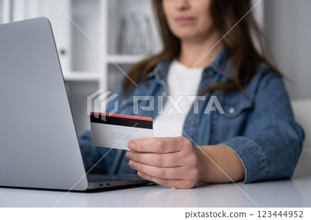A woman is actively engaged in online shopping, utilizing her credit card and laptop to make purchases from the comfort of her home, embracing modern retail technology for convenience A woman is actively engaged in online shopping, utilizing her credit card and laptop to make purchases from the comfort of her home, embracing modern retail technology for convenience 123444952