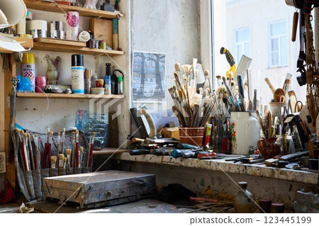Creative workspace filled with various tools and brushes in a sunlit studio setting 123445199
