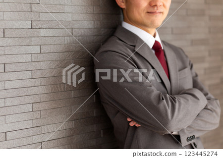 一位身穿灰色西裝的中年男性商人雙手交叉靠在牆上 123445274