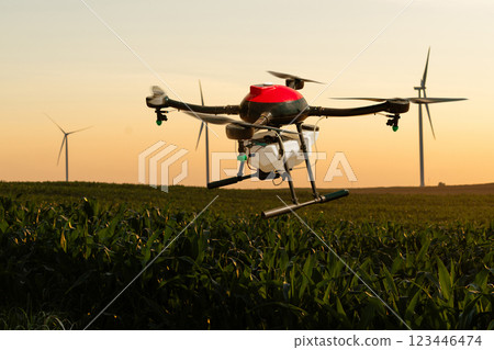 Drone sprayer flies over the agricultural field. Wind turbines on a horizon.Drone sprayer flies over the agricultural field. Wind turbines on a horizon 123446474