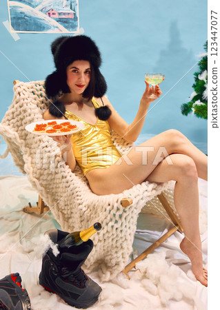 Relaxed woman in golden swimsuit reclining on cozy chair with caviar and champagne against abstract winter studio background Relaxed woman in golden swimsuit reclining on cozy chair with caviar and champagne against abstract winter studio background 123447077