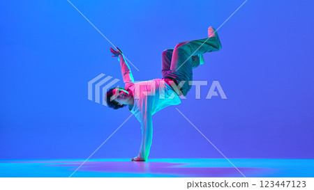 Skilled young male dancer captured in mid-motion, showing breakdance technique against gradient blue purple background in neon light 123447123