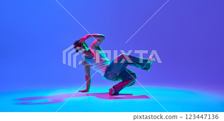 Talented and skilled young guy in casual clothes in motion, dancing breakdance against gradient blue purple background in neon light Talented and skilled young guy in casual clothes in motion, dancing breakdance against gradient blue purple background in neon light 123447136