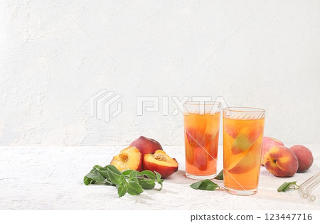 Iced peach tea or cocktail with mint and lobdom,recipe for refreshing summer drink.Two glasses with peach fruit lemonade on light concrete table,detox diet and weight loss concept,menu for Iced peach tea or cocktail with mint and lobdom,recipe for refreshing summer drink.Two glasses with peach fruit lemonade on light concrete table,detox diet and weight loss concept,menu for 123447716