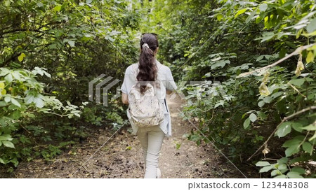 Young woman going along path at summer forest. Female with backpack walking among trail at wild nature. Unrecognizable girl enjoying stroll outdoor admiring beautiful scenic. Close up Rear view Young woman going along path at summer forest. Female with backpack walking among trail at wild nature. Unrecognizable girl enjoying stroll outdoor admiring beautiful scenic. Close up Rear view 123448308