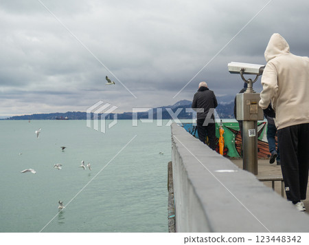 Man on the pier against the backdrop of seagulls. People feed the seagulls. Beautiful seascape in cloudy weather Man on the pier against the backdrop of seagulls. People feed the seagulls. Beautiful seascape in cloudy weather 123448342