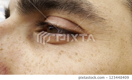 Focus on left brown eye of handsome sorrowful man looking into the distance. Portrait of unhappy male face with freckles outdoor. Upset facial expression of young guy. Close up 123448409