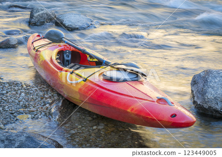 whitewater kayak on a river shore with a rapid in background 123449005
