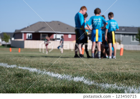 Selective focus on flag football grass with blurred youth team huddle in the background 123450715