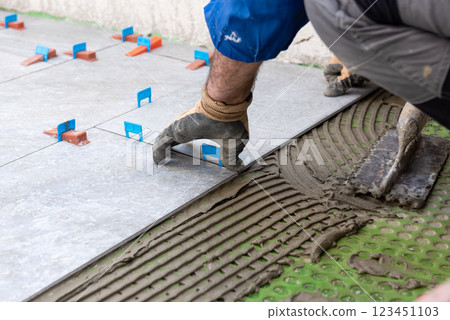 Tiler at work installing new floor with tiles. Construction. 123451103