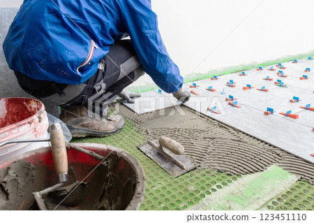 Tiler at work installing new floor with tiles. Construction. Tiler at work installing new floor with tiles. Construction. 123451110
