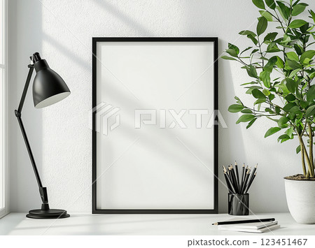 A black picture frame offers blank copy space on a white desk with a lamp and plant. 123451467