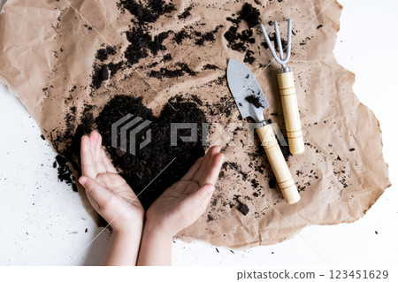 Child hands shaping soil heart with garden tools on brown paper 123451629