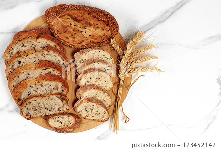 Freshly baked whole grain homemade sourdough bread with crispy crust, sliced and ears of wheat on marble background, modern baking concept, healthy natural food 123452142