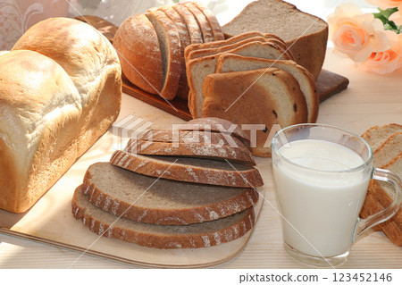 A loaf, slices of fresh bread and a cup of milk on a sunny table. Healthy food  123452146
