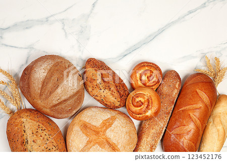 Freshly baked whole grain homemade bread, different types of round sourdough bread with crispy crust, baguettes, buns and ears of wheat on marble background, modern baking concept, 123452176