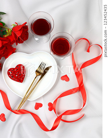 Festive table setting, menu layout for Valentine's Day, cutlery with a heart on a plate and glasses with wine, festive composition with a bouquet of red roses, kitchen background. Selective focus Festive table setting, menu layout for Valentine's Day, cutlery with a heart on a plate and glasses with wine, festive composition with a bouquet of red roses, kitchen background. Selective focus 123452435