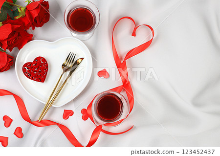 Festive table setting, menu design for Valentine's Day, cutlery with a heart on a plate and glasses with red wine, festive composition with a bouquet of red roses, kitchen background. Selective focus 123452437